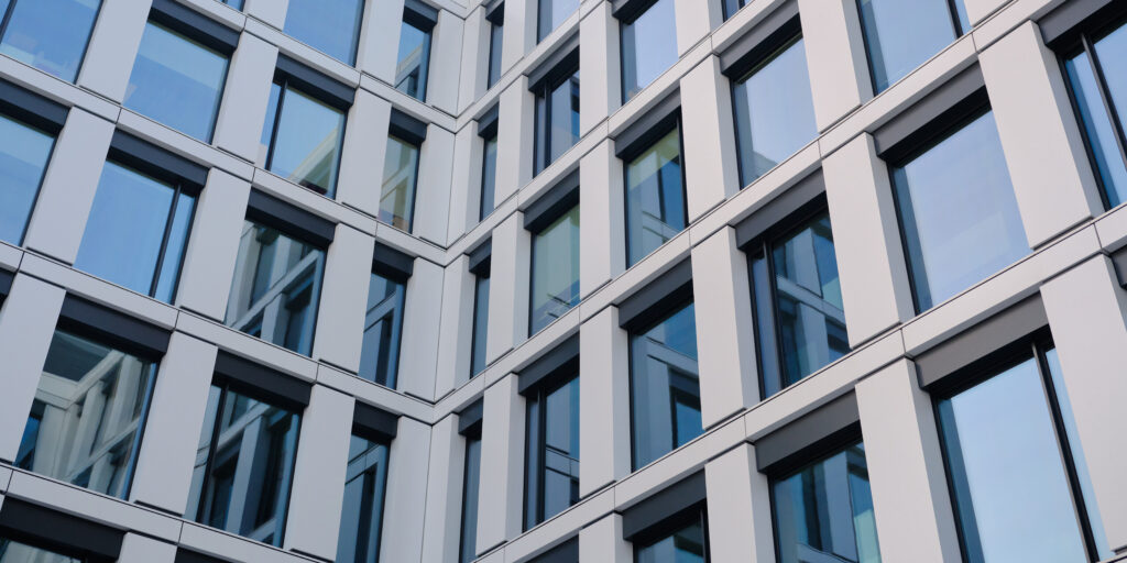 Modern office building facade with glass windows and metal panels forming a clean geometric pattern, contemporary architecture background for corporate and design use.